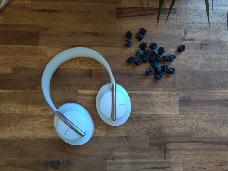 Bose NC700 headphones on a desk next to some keyboard switches