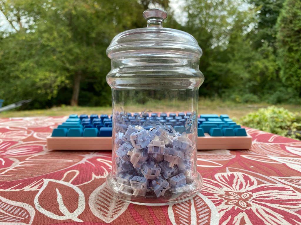 A jar of mechanical switches in front of a keyboard.